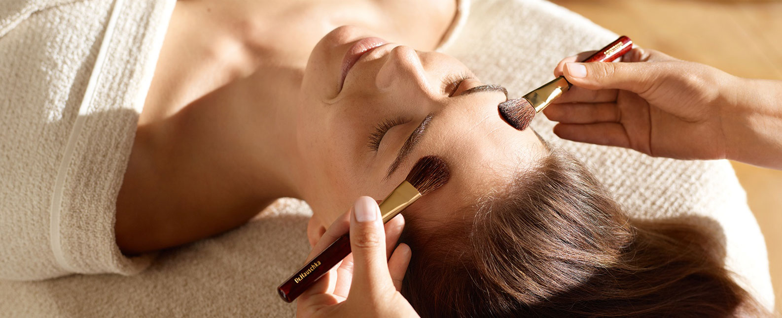Entspannt liegende Frau bekommt Behandlung mit Pinseln im Gesicht